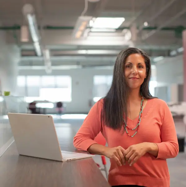 Woman in professional clothing inside an office, standing in front of a computer